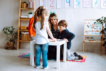 Group of amazing children studying with help of teacher woman in classroom. Pupils learning board games. Education.