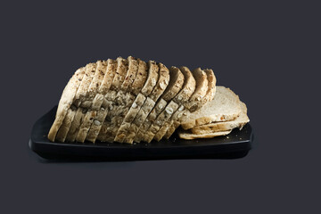 Loaf of multigrain bread on black platter isolated on black background. sliced bread