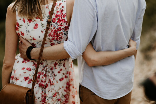A couple in love are walking and cuddling as they walk. Romantic outdoor date. Happy relationship, active lifestyle. Fashionable trendy clothes, leather purse bag. Hugging each other with hands. 