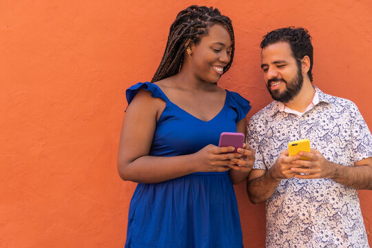 Multiethnic couple browsing smartphones against orange background