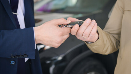 An unrecognizable manager shakes hands with a client and hands over the car key. The transaction went through, the buyer and the seller are satisfied.