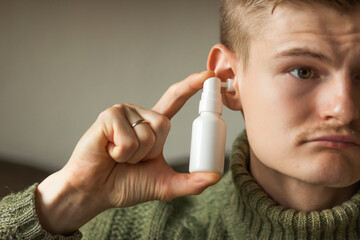Man uses an ear spray. Man's hand holds a white ear spray bottle with nozzle installed in the ear...