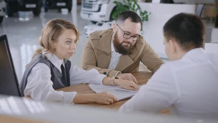 A married couple buys a new car in a car dealership. A man and a woman look at the contract and conditions. - Powered by Adobe