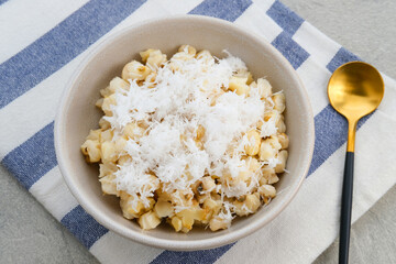 Grontol Jagung or Corn grontol is a traditional snack in Indonesia. Boiled shelled corn sprinkled with grated coconut. Served in a bowl on grey background.