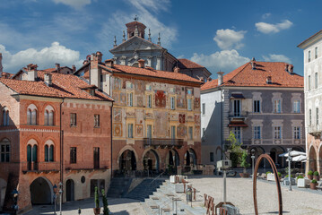 Mondovì, Cuneo, Piedmont, Italy - August 08, 2022:  Ancient medieval buildings with mullioned windows with frescoed brick facades and cathedral in Piazza Maggiore in the ancient Piazza district