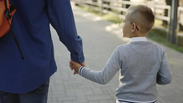 Male person taking his son to school. Father holding son hand and telling father stories from school biology lesson. Focus on boy. Concept of education and family