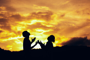 Fototapeta na wymiar Silhouette of two people praying and worship to God at sunset. Hands in prayer. Christian Religion concept background. Copy space for your individual text.