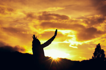 Silhouette of a woman raised hands praying to God at sunset. Christian Religion concept background. Copy space for your individual text.