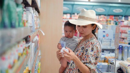 Young modern single mother choosing baby cream in supermarket