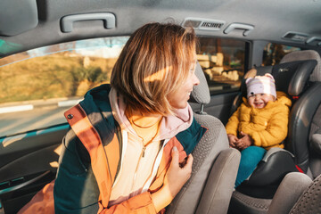 Smiling mother looking back to her cute happy little child is sitting at safe childrens backseat. The concept of safety during travel by car