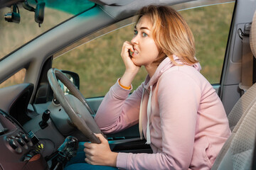 A scared nervous woman is sitting behind the wheel of a car and bites her nails. Side view. Fine...