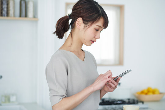 キッチンでスマートフォンを使う女性