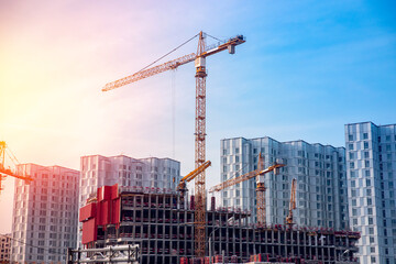 Construction site of modern apartment buildings with steel structures and cranes against blue sky with sun glare