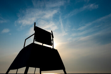 The dark outlines of a tall lifeguard observation chair on the beach. Photo taken against the sun...