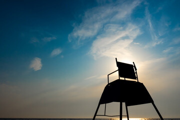 The dark outlines of a tall lifeguard observation chair on the beach. Photo taken against the sun...