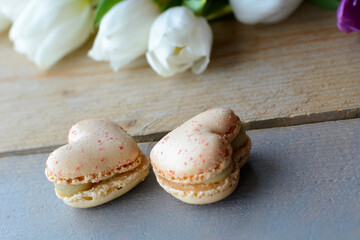 Two creamy macarons are lying on the wooden table. Two macarons in form of the heart. Dessert is on the wood