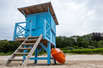 A blue lifeguard booth on the beach on a cloudy day. Orange lifeboat leaning against the side of...