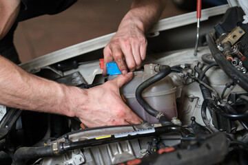 Fototapeta na wymiar Car mechanic hands opening or closing antifreeze container. Mechanics workshop.