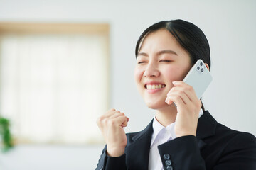 スマートフォンを持ち喜ぶスーツを着た若い女性