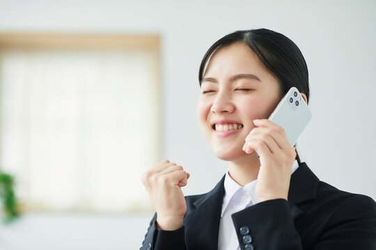 スマートフォンを持ち喜ぶスーツを着た若い女性