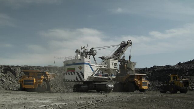 Group of technological transport around huge mining excavator. Two dump trucks and small loader