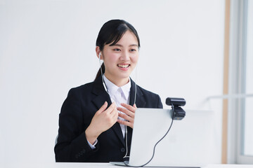 ノートパソコンのカメラに向かって話す笑顔のスーツを着た若い女性