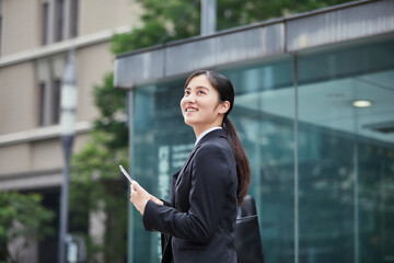 オフィス街でスーツを着てスマートフォンを持つ若い女性
