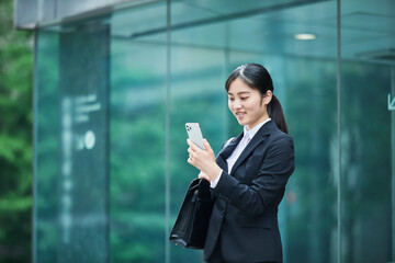 オフィス街でスーツを着てスマートフォンを持つ若い女性
