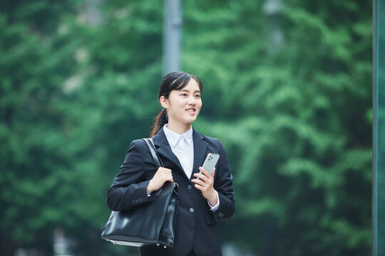 オフィス街でスーツを着てスマートフォンを持つ若い女性