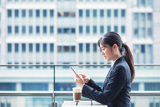 オフィス街のカフェでスーツを着てスマートフォンを持つ若い女性