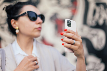 A woman's hand with red manicure holding a pink smartphone. Woman in sun glasses looking at her phone 