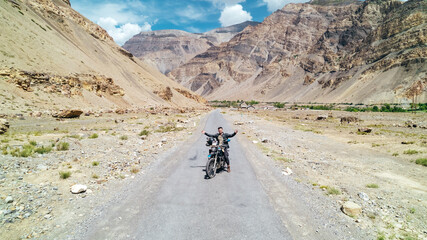 dry desolate Himalayan Mountain terrain in Spiti Valley India with man riding motorcycle on empty desert road