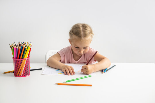 Blonde child girl draws with colored pencils sitting at the table