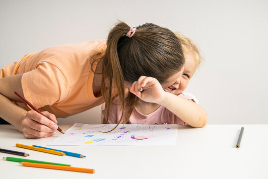 Joyful hugging mom and child girl draw together with colored pencils on paper