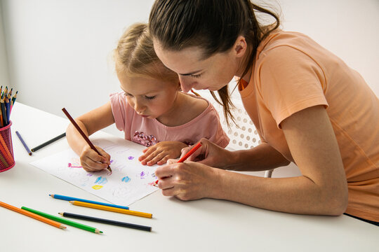 Child girl with mom draw with colored pencils on white paper