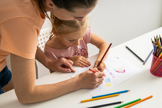 Mom and daughter draw together with colored pencils on paper at the table