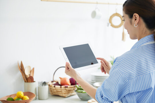 キッチンでタブレットPCを見ながら料理を作る女性