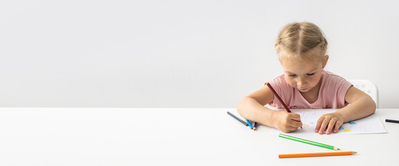 Blonde child girl draws with colored pencils sitting at the table. Banner