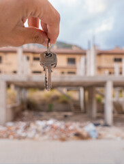 Detalle de mano con las llaves, en una finca en construcci&oacute;n de segundo plano. Fotograf&iacute;a vertical, con espacio para texto.