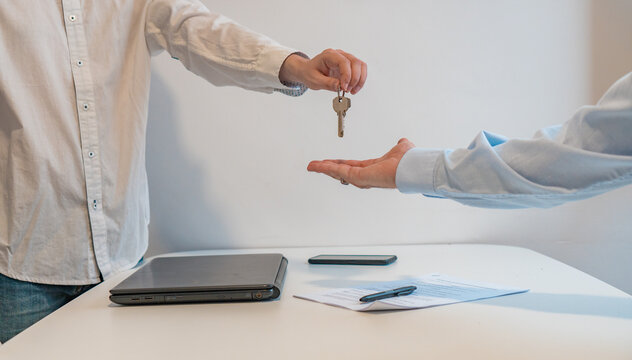 Detalle de manos de agente dando las llaves al comprador, en la inmobiliaria. Fotografía horizontal con espacio para texto.