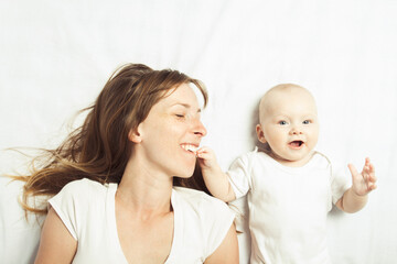 Young mother plays with her baby on a bed with a white sheet. Flat lay, top view
