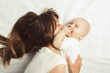 Young mother plays with her baby on a bed with a white sheet. Flat lay, top view