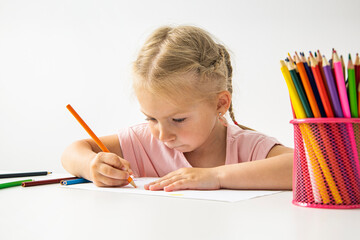 A child blonde girl draws with colored pencils sitting at the table