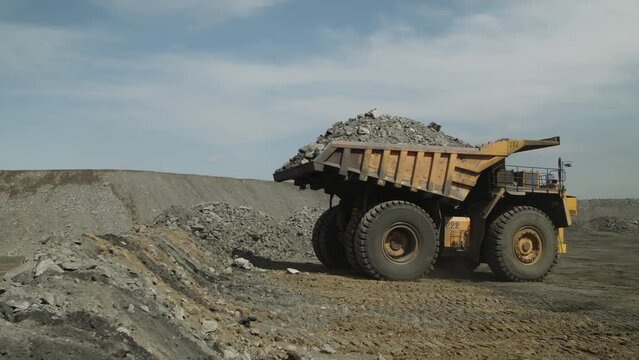 Multi-ton dump truck lifts body, unloads waste rock and leaves. Element of coal mining process. Panoramic view