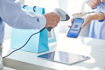 スマートフォンを持ちキャッシュレス決済をする女性の手元と店員の手