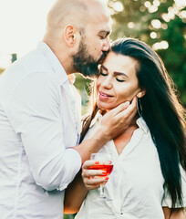 Portrait of a Smiling  happy Couple Kissing    in a Vineyard toasting wine. Beautiful  brunette woman and bearded muscular man spending time together during grape harvest.