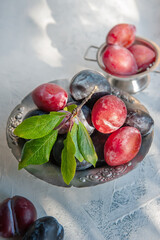 antique silver bowl filled with red plums on a rustic table. photographed in natural light in real life.