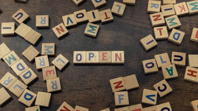 OPEN. The word open created by square wooden puzzles with painted letters. Other unarranged letters surrounding the word. High quality 4k footage