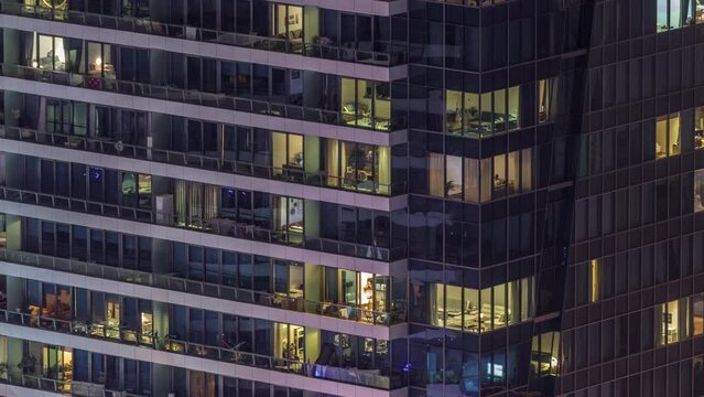 Windows lights in modern office and residential buildings timelapse at night. Multi-level skyscrapers with illuminated rooms inside. Some people on a balconies