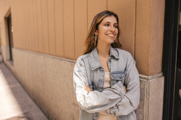 Positive young caucasian woman spends free time on walk in sunny weather spring. Brown-haired girl with snow-white smile wears denim jacket. Lifestyle concept